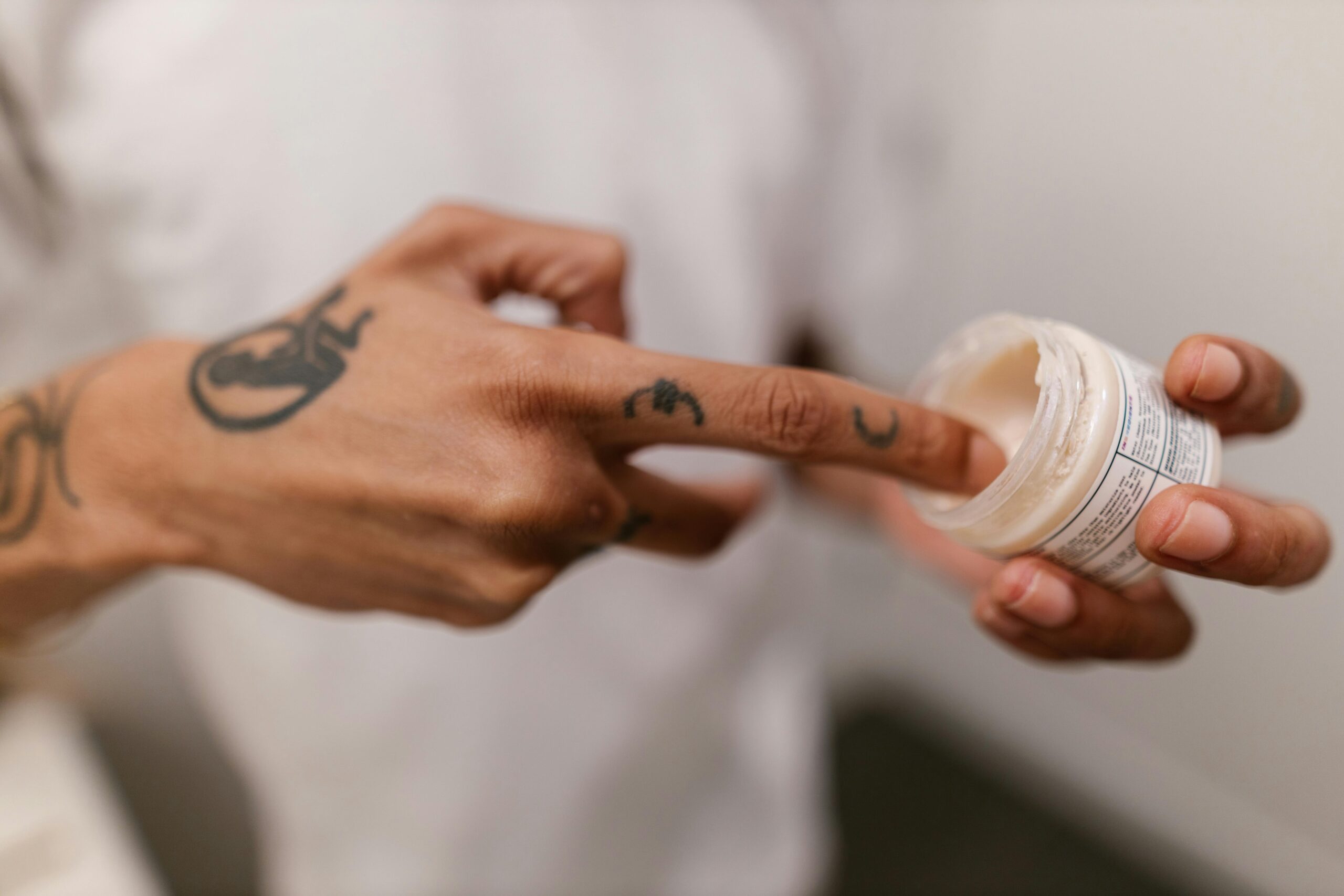 Close-up of hands applying moisturizer to skin with a gaming tattoo visible