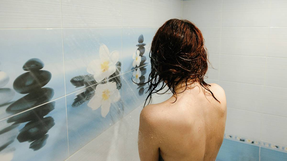 A model wearing a clear waterproof covering over their forearm tattoo while taking a shower.