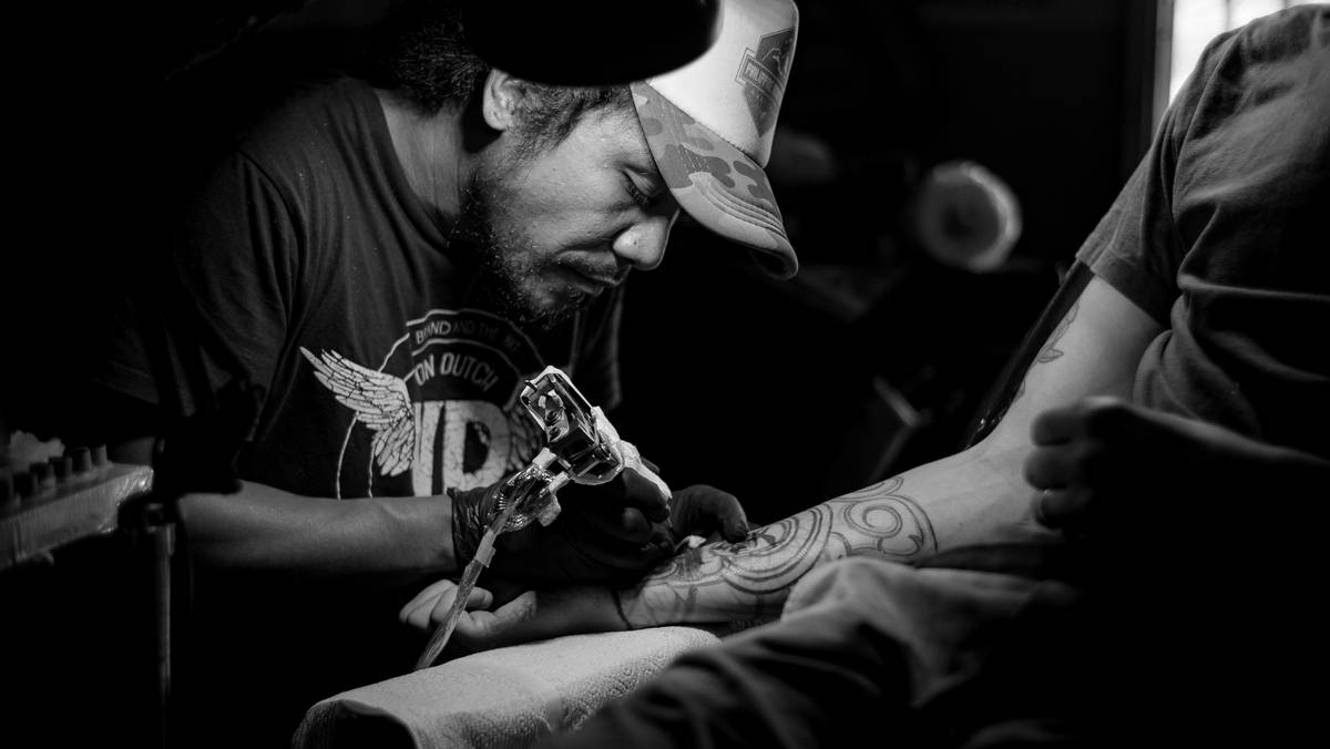 Tattoo artist Resident Evil working on a detailed black-and-gray biohazard symbol with subtle vine motifs