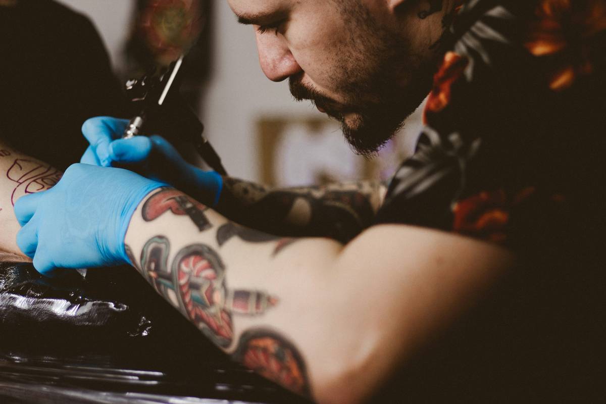 tattoo artist Sekiro sketching a detailed gaming tattoo design featuring prosthetic tools and sakura branches